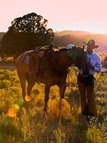 RubEn Mizquez stands next to a saddled horse in a pasture.